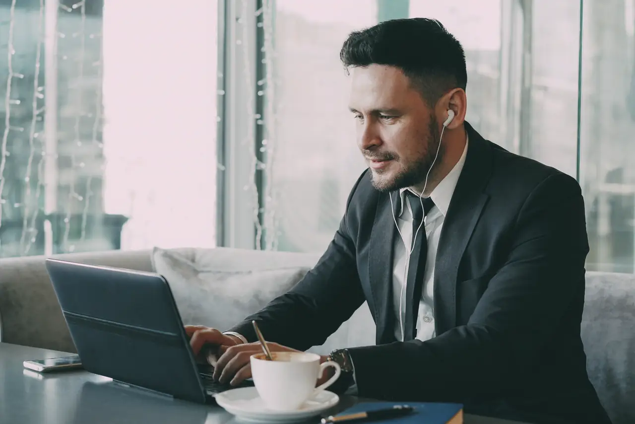 Professional works on a laptop at a cafe table wearing earbuds