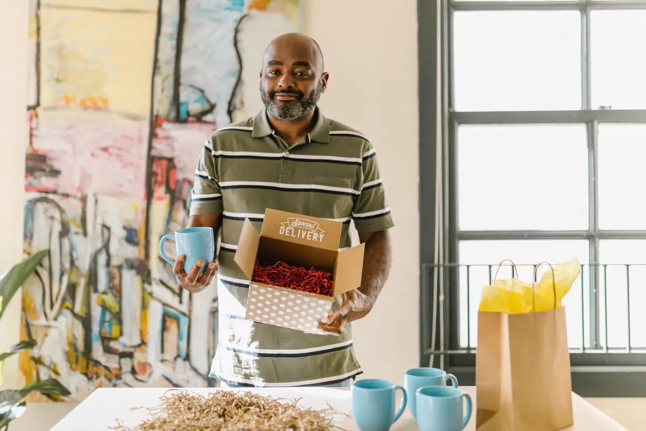 Shop owner packs blue coffee mugs into a box for delivery in a bright workspace