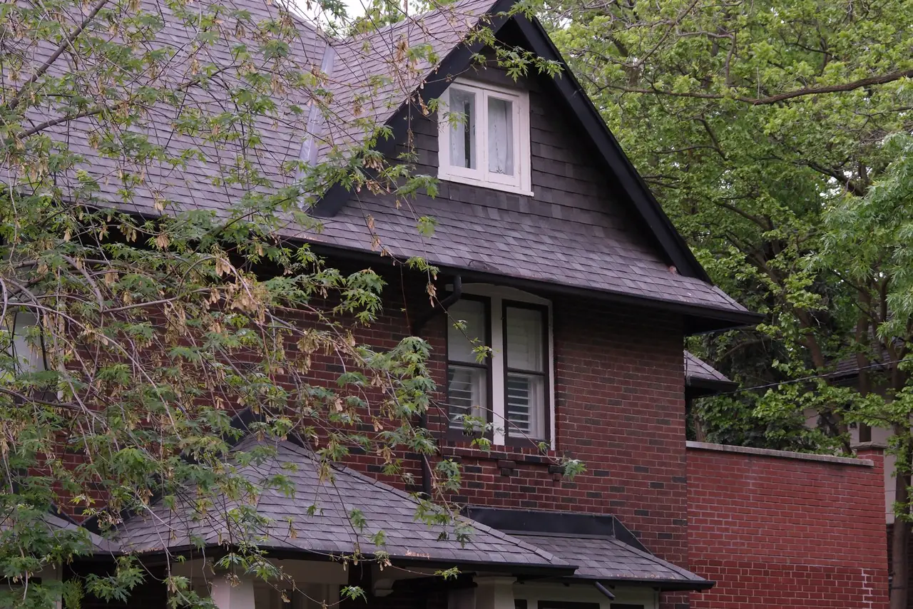 Brick house surrounded by green trees and shrubs in a Toronto neighbourhood