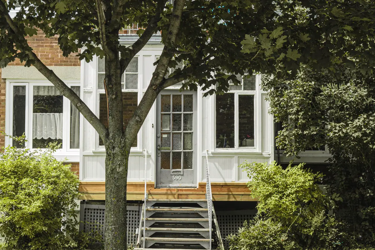 White family house with a porch and leafy garden in a quiet Quebec City street
