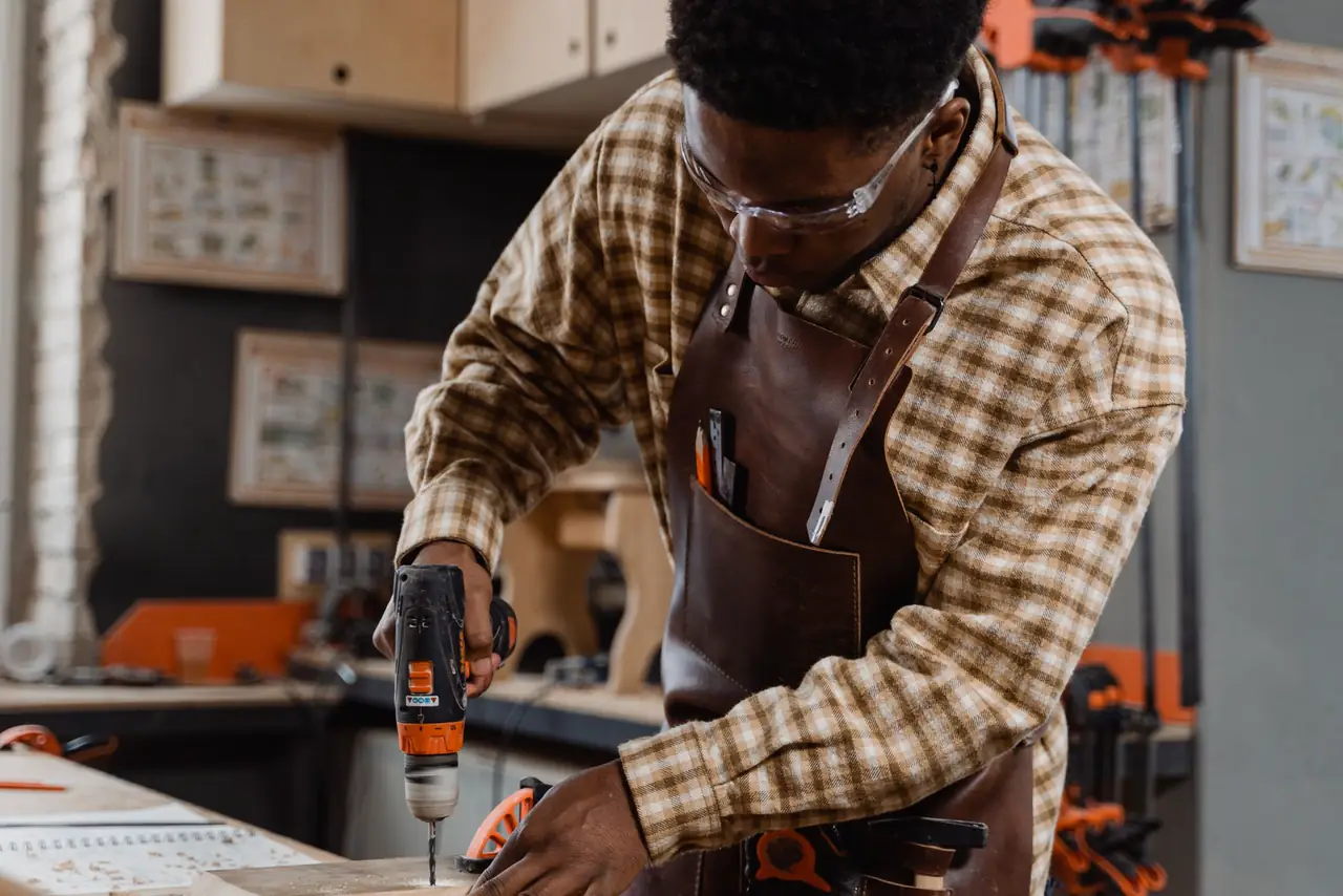 Craftsman in safety goggles and an apron drills into timber in his workshop