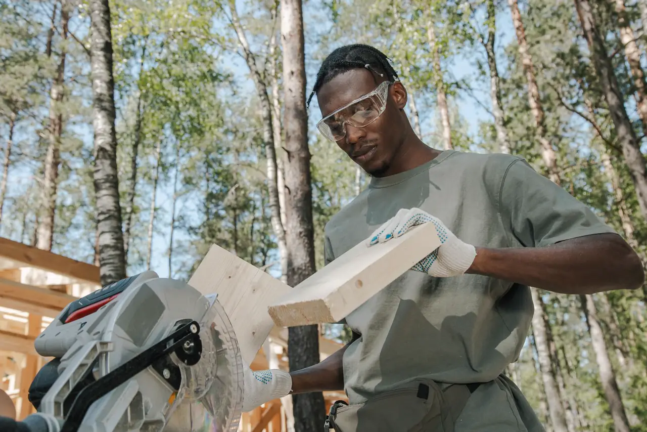 Tradesperson in safety gear cuts timber outdoors with a power saw
