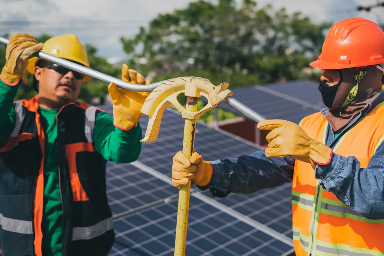 Two workers in high visibility gear assemble solar panel equipment in bright sunshine